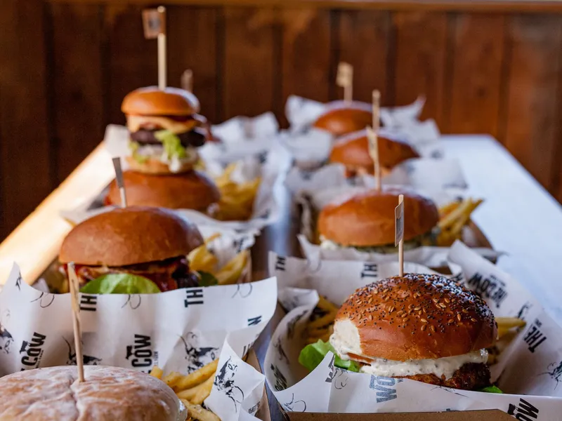 A row of gourmet beef burgers and chips served in paper-lined trays on a table at The Cow, Tapnell Farm, Isle of Wight.