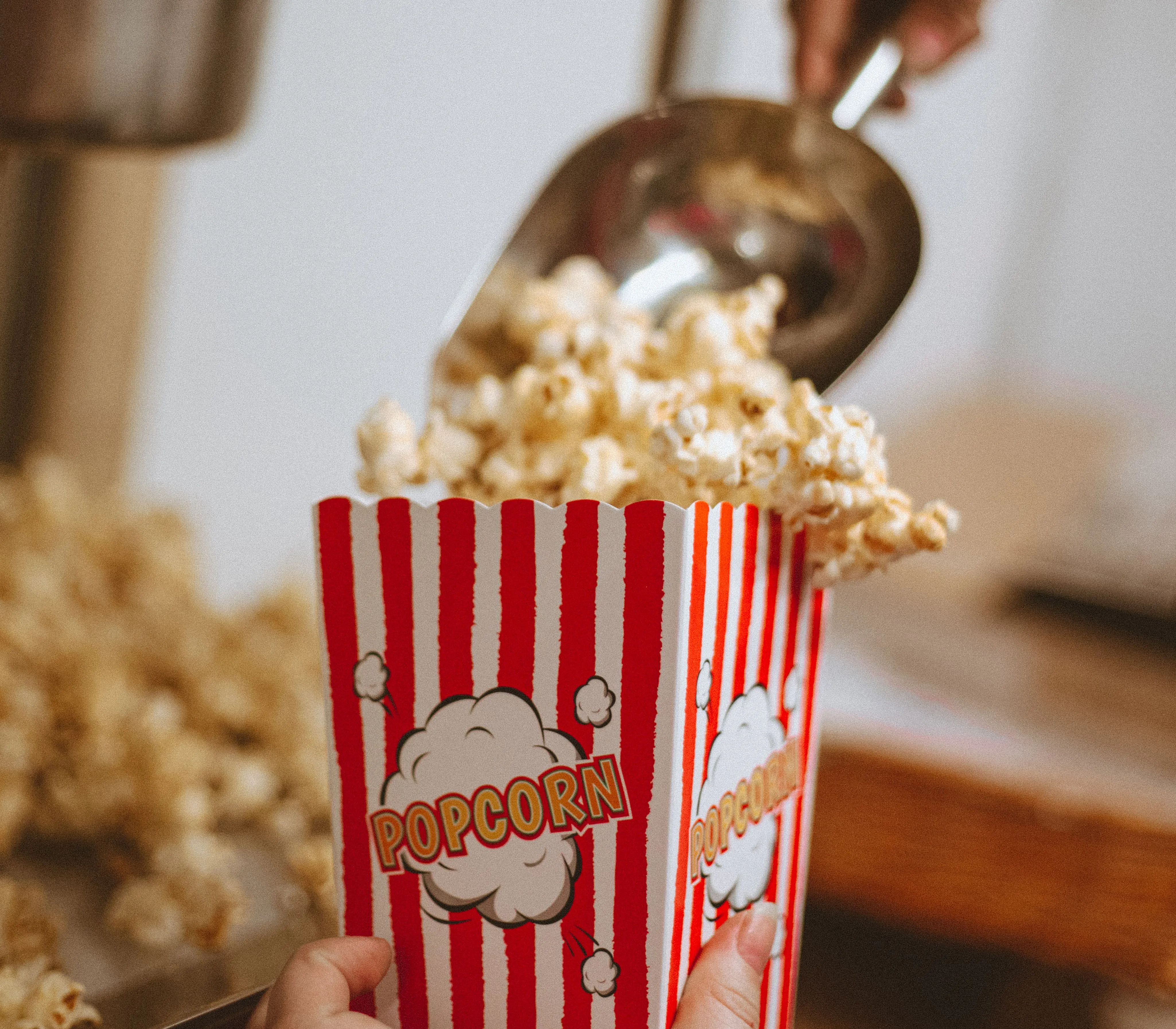 Fresh popcorn being scooped into a red-and-white striped popcorn box