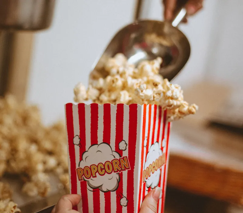 Fresh popcorn being scooped into a red-and-white striped popcorn box