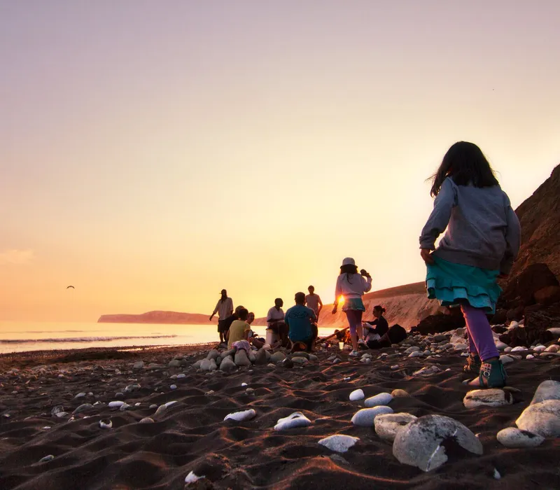 Group of people on a rocky beach at sunset with a child in the foreground