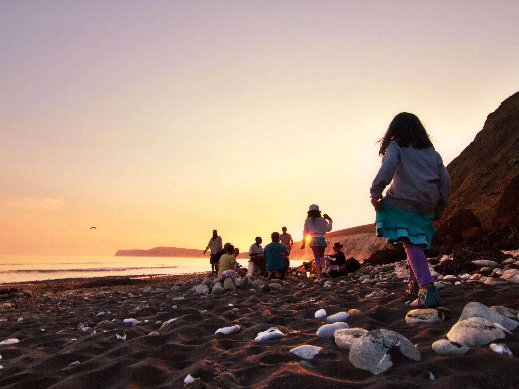 Group of people on a rocky beach at sunset with a child in the foreground