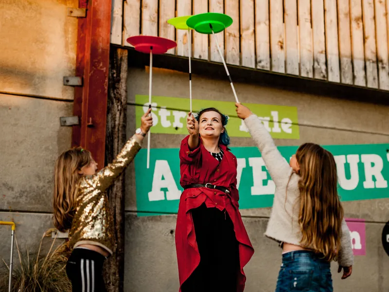Three people performing a plate-spinning act outdoors, holding spinning sticks with colourful plates