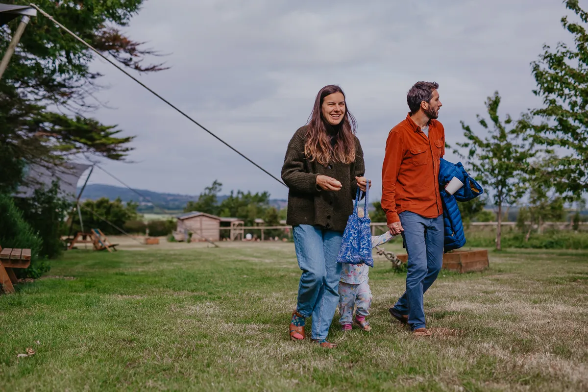 A couple walk across a grassy garden with a small child between them on a cloudy day.