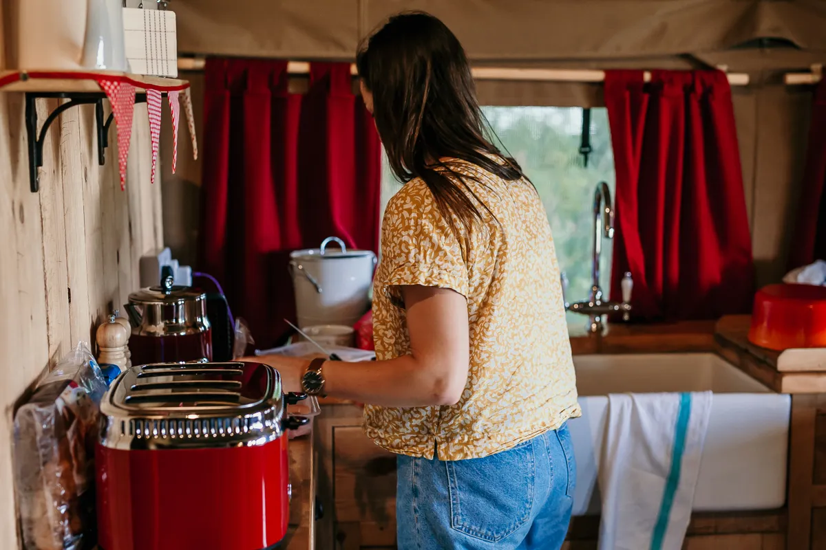 Woman preparing food in a cosy cabin kitchen with red curtains and a red toaster