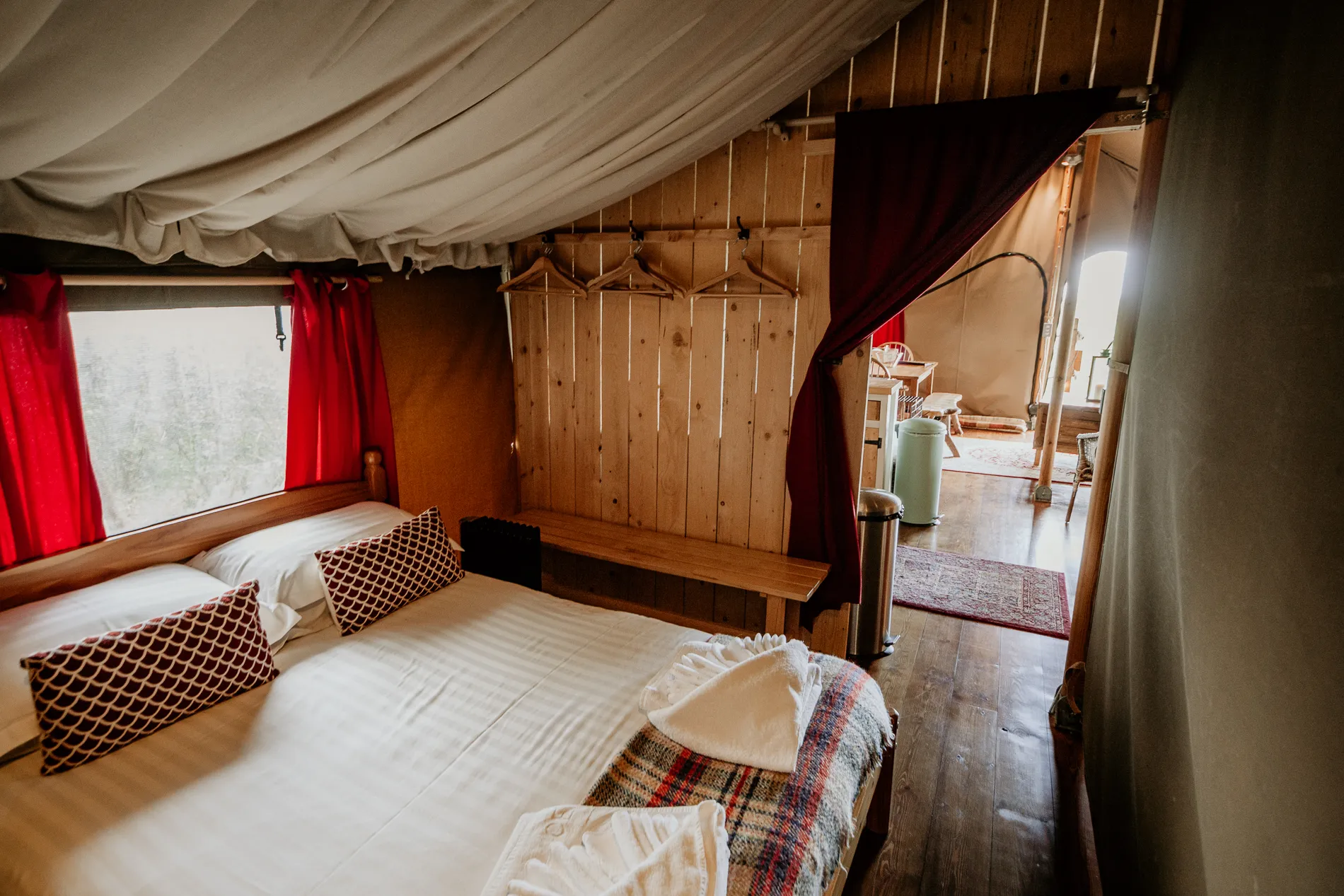 Cosy safari tent bedroom with double bed, red curtains and wooden interior