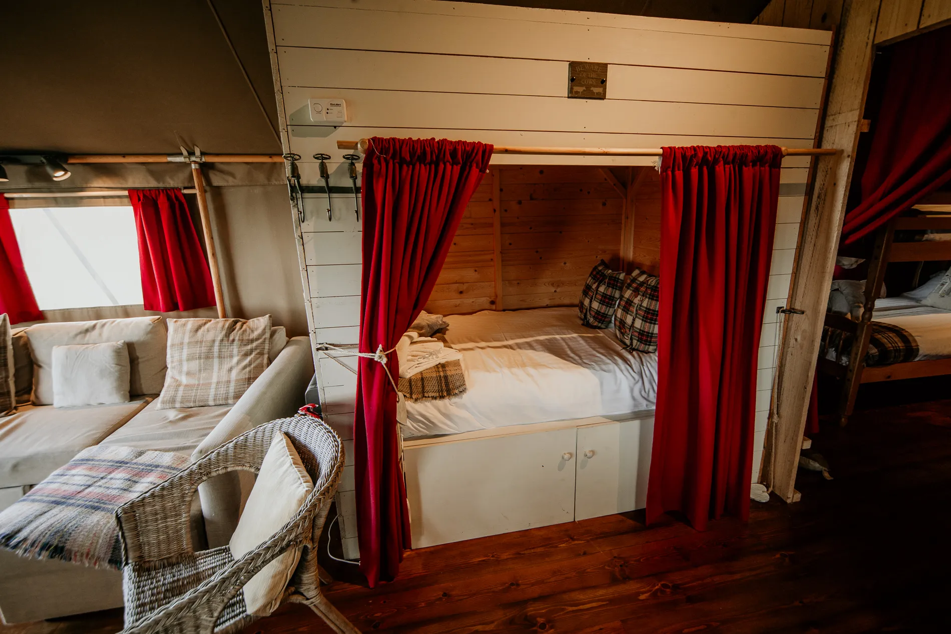 Cosy safari tent bedroom with a curtained alcove bed, plaid cushions and wooden bunk beds.