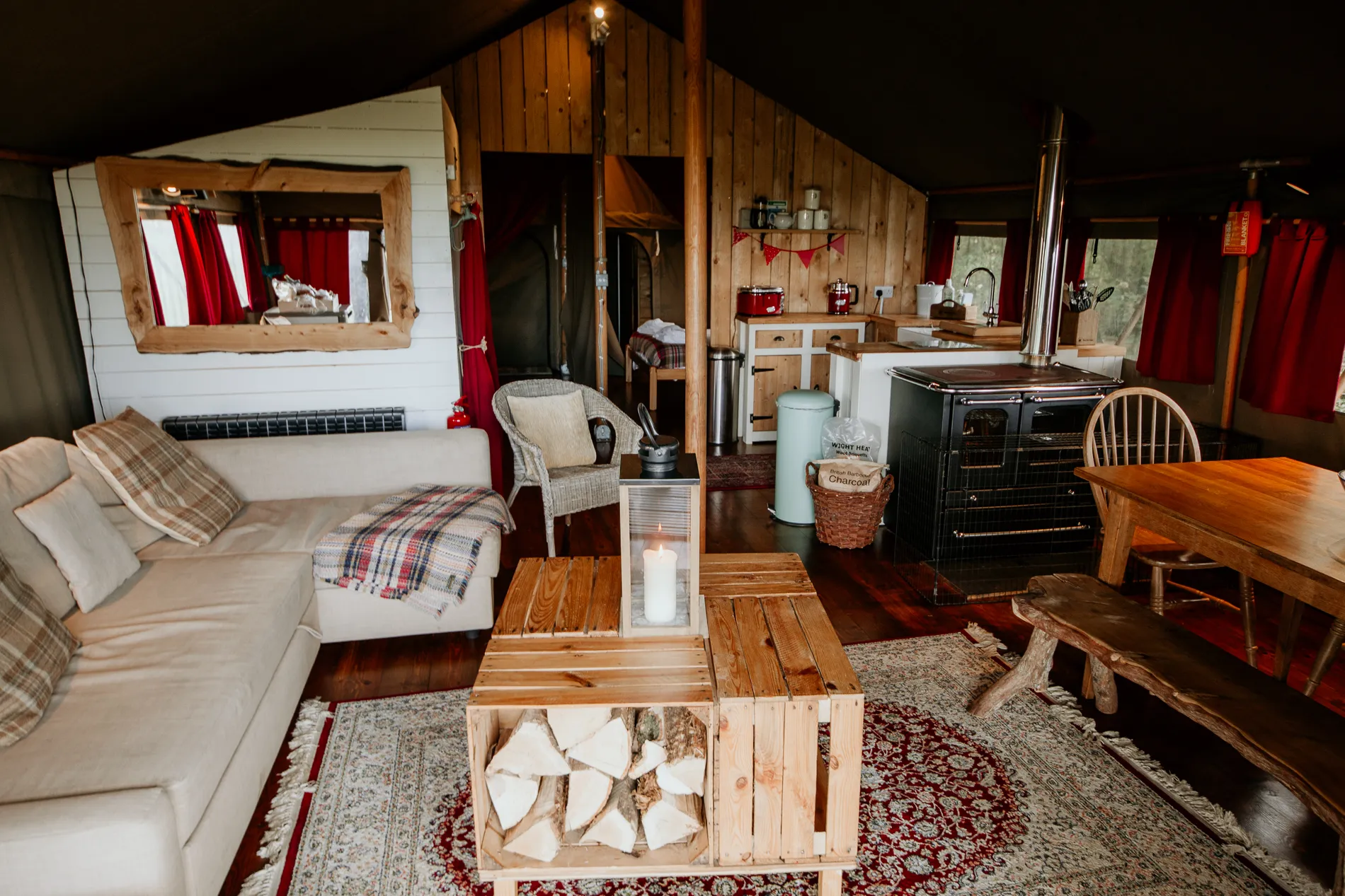 Cosy safari tent interior with sofa, wood-burning stove, kitchenette and wooden dining table