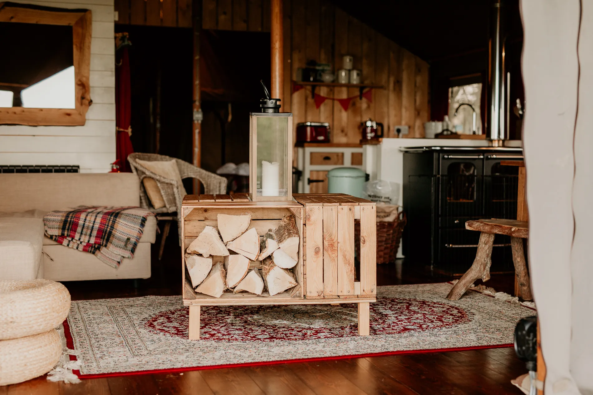 Cosy safari tent interior with rustic wooden stove, log store and small kitchenette