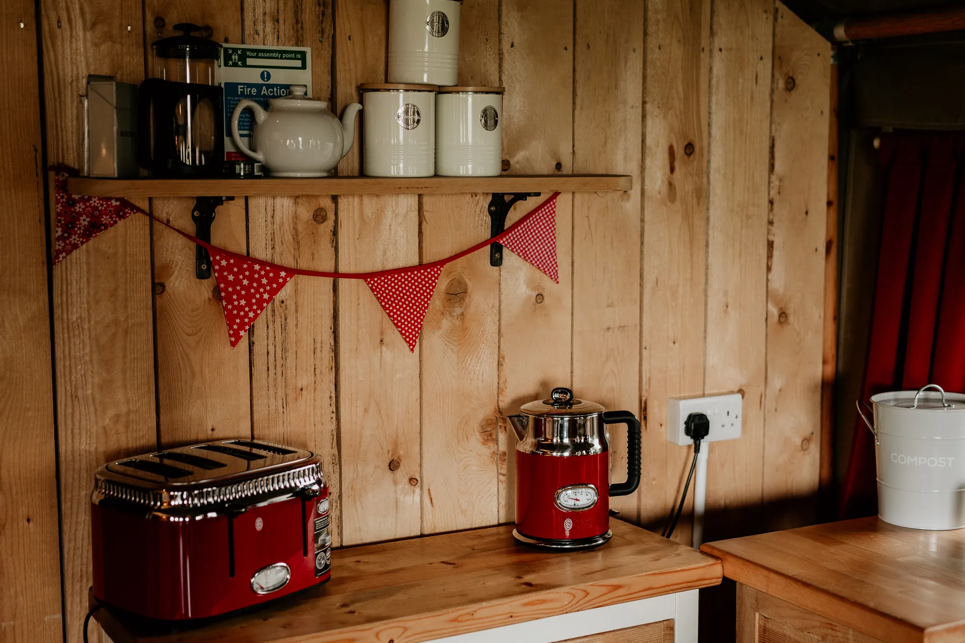 Rustic safari tent kitchenette with red toaster and kettle, wooden shelves and bunting