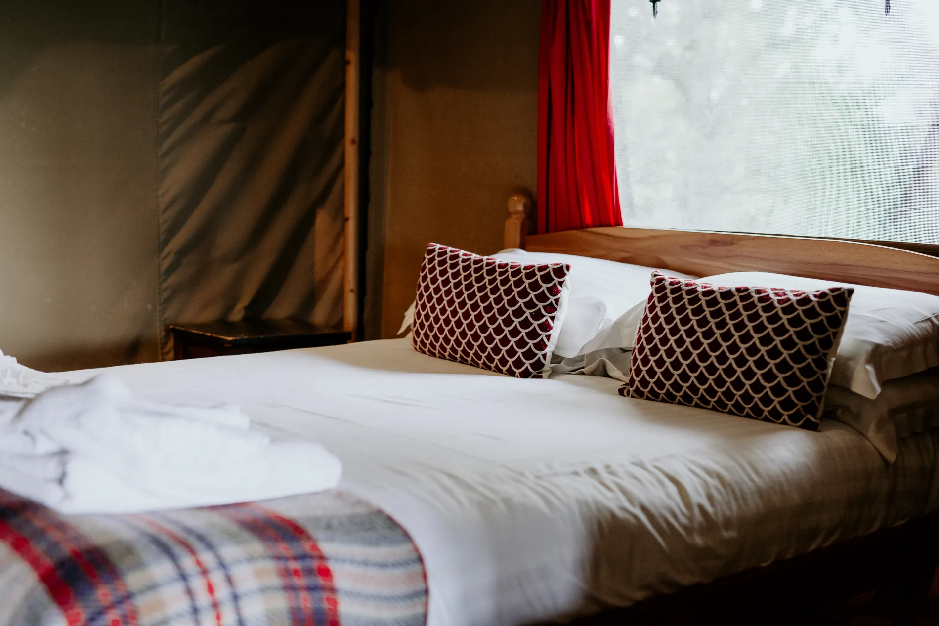 Cosy bed inside a safari tent with red patterned cushions and a tartan blanket
