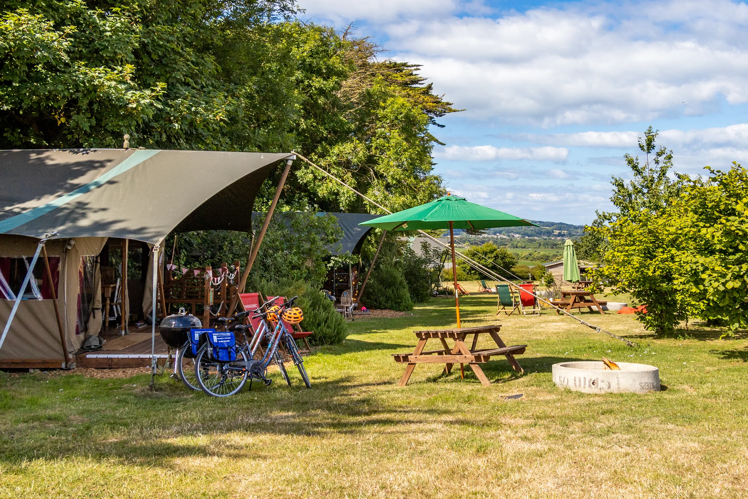 Safari tents with picnic benches and bicycles on a grassy glamping field