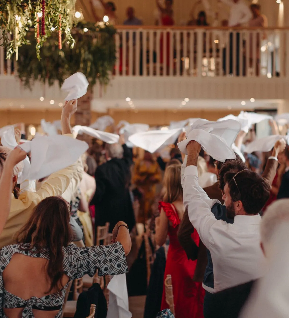 Wedding guests waving white napkins during a lively reception in a bright indoor venue