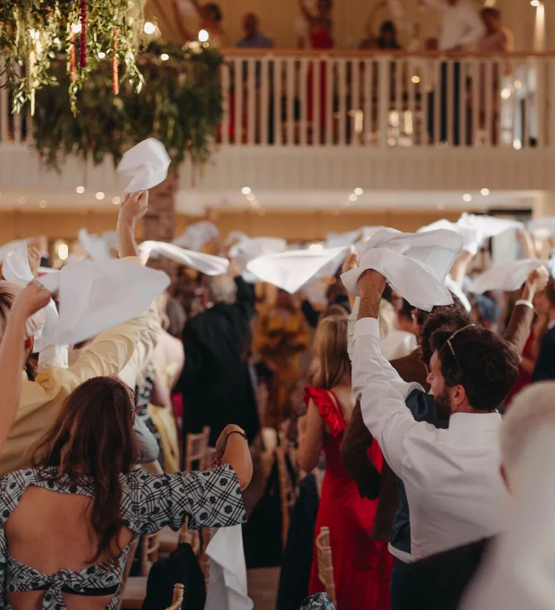 Wedding guests waving white napkins during a lively reception in a bright indoor venue