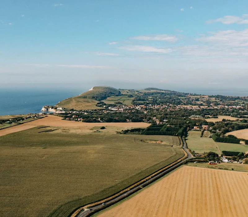 Aerial view of coastal countryside with patchwork fields, a headland and sea under a blue sky
