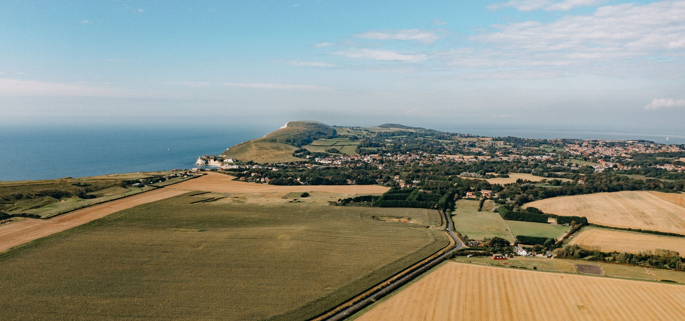 Aerial view of coastal countryside with patchwork fields, a headland and sea under a blue sky