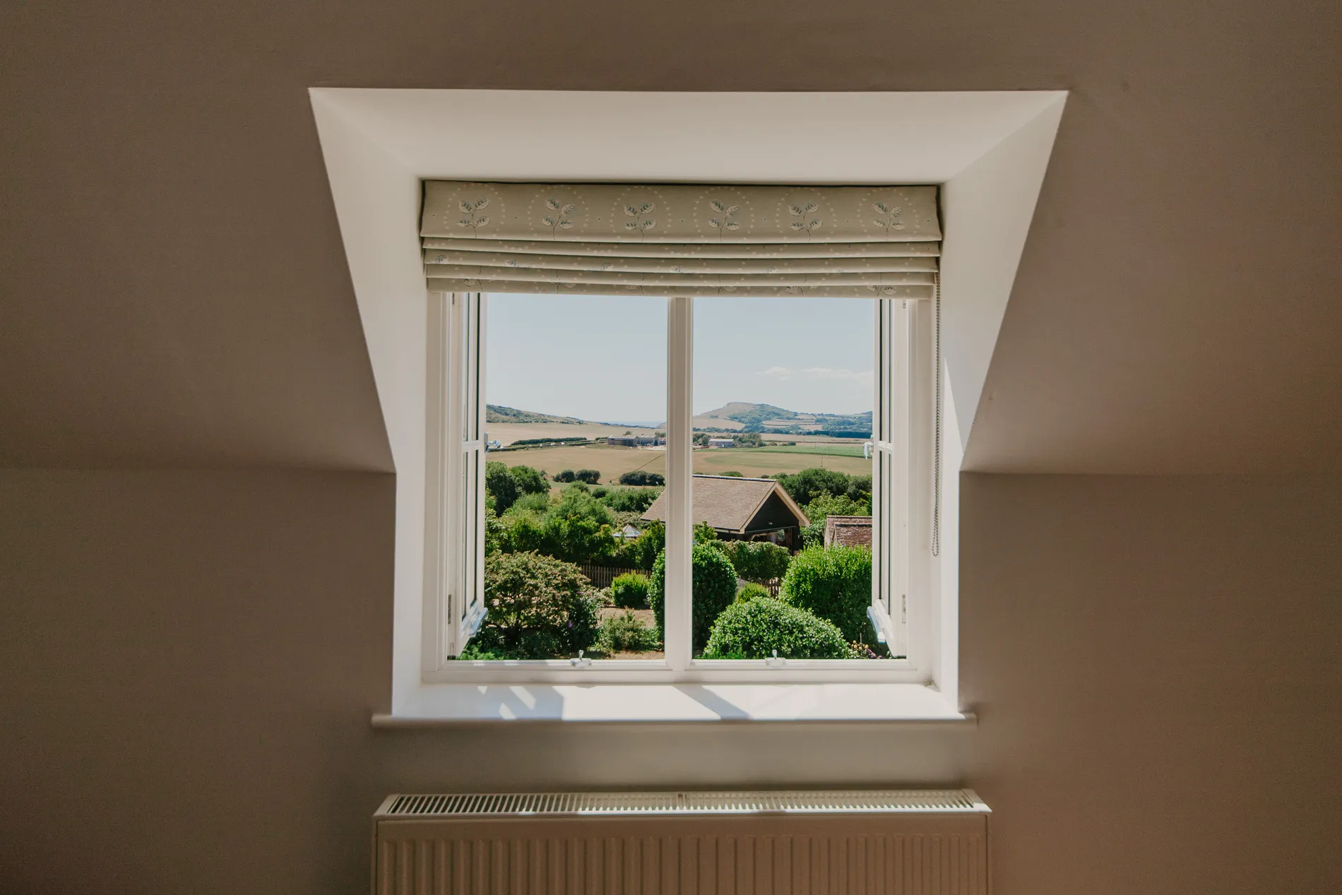 View through a cottage window over green countryside fields and distant hills on a sunny day
