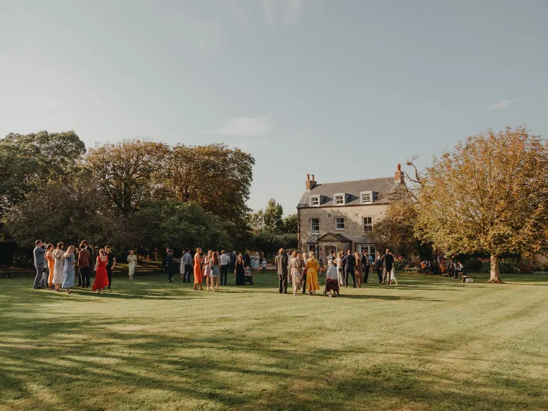 Wedding guests gathered on a lawn outside a country house in late afternoon light