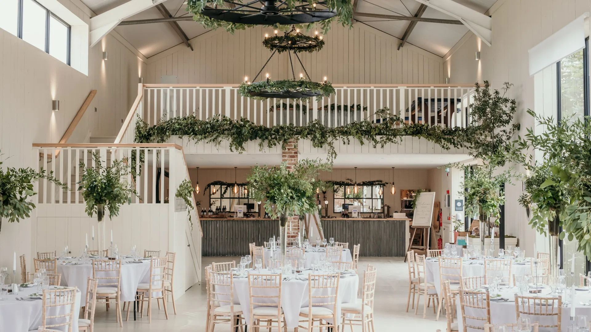 Interior of East Afton Farmhouse events barn with mezzanine, greenery garlands and round dining tables set for a reception