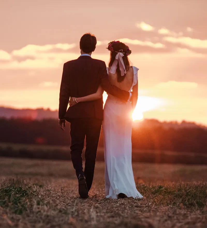 Bride and groom walking arm in arm through a field at sunset