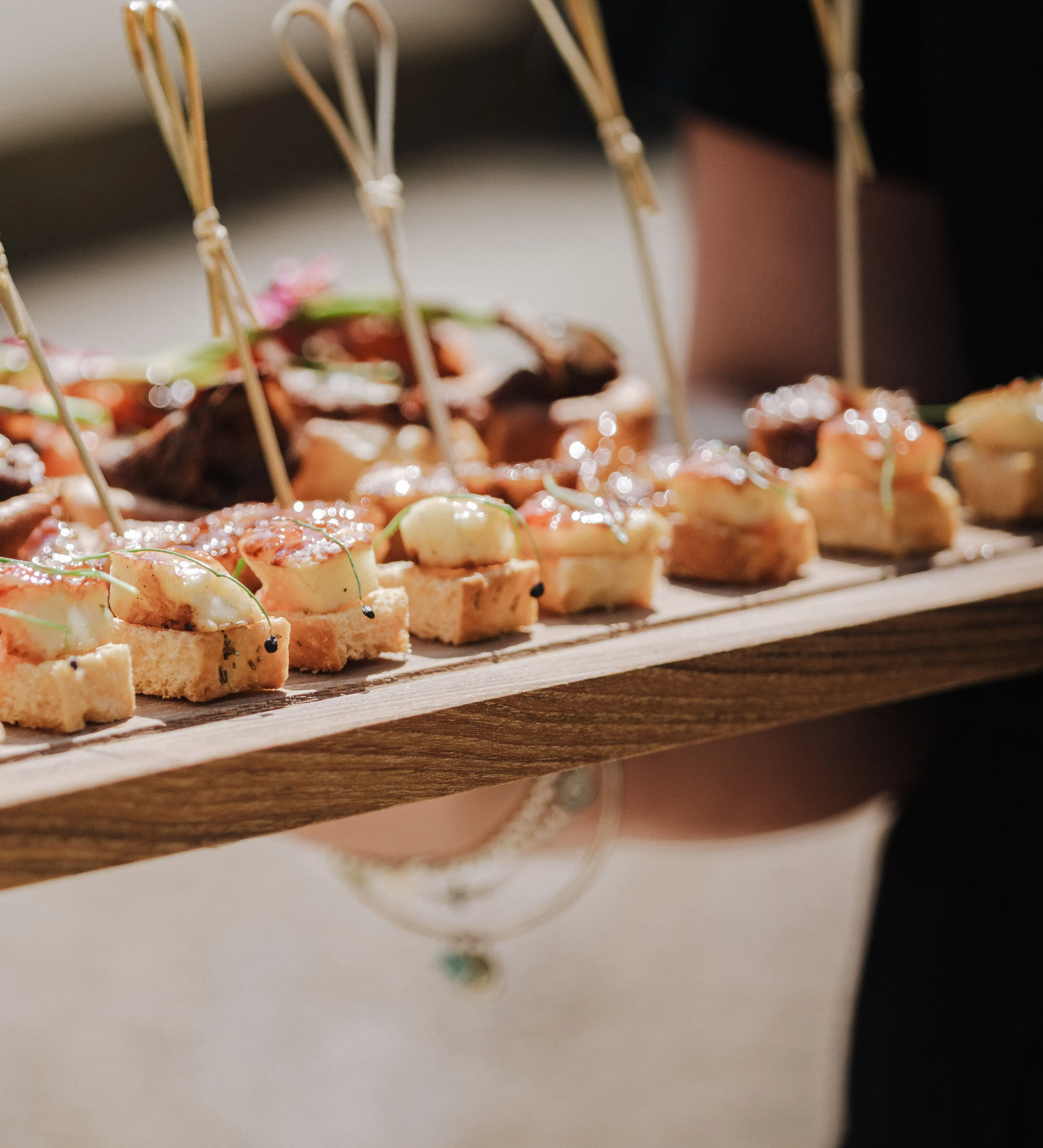 Close-up of a wooden platter of wedding canapés with small skewers
