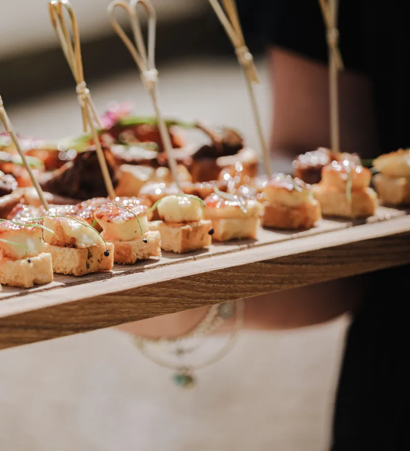 Close-up of a wooden platter of wedding canapés with small skewers