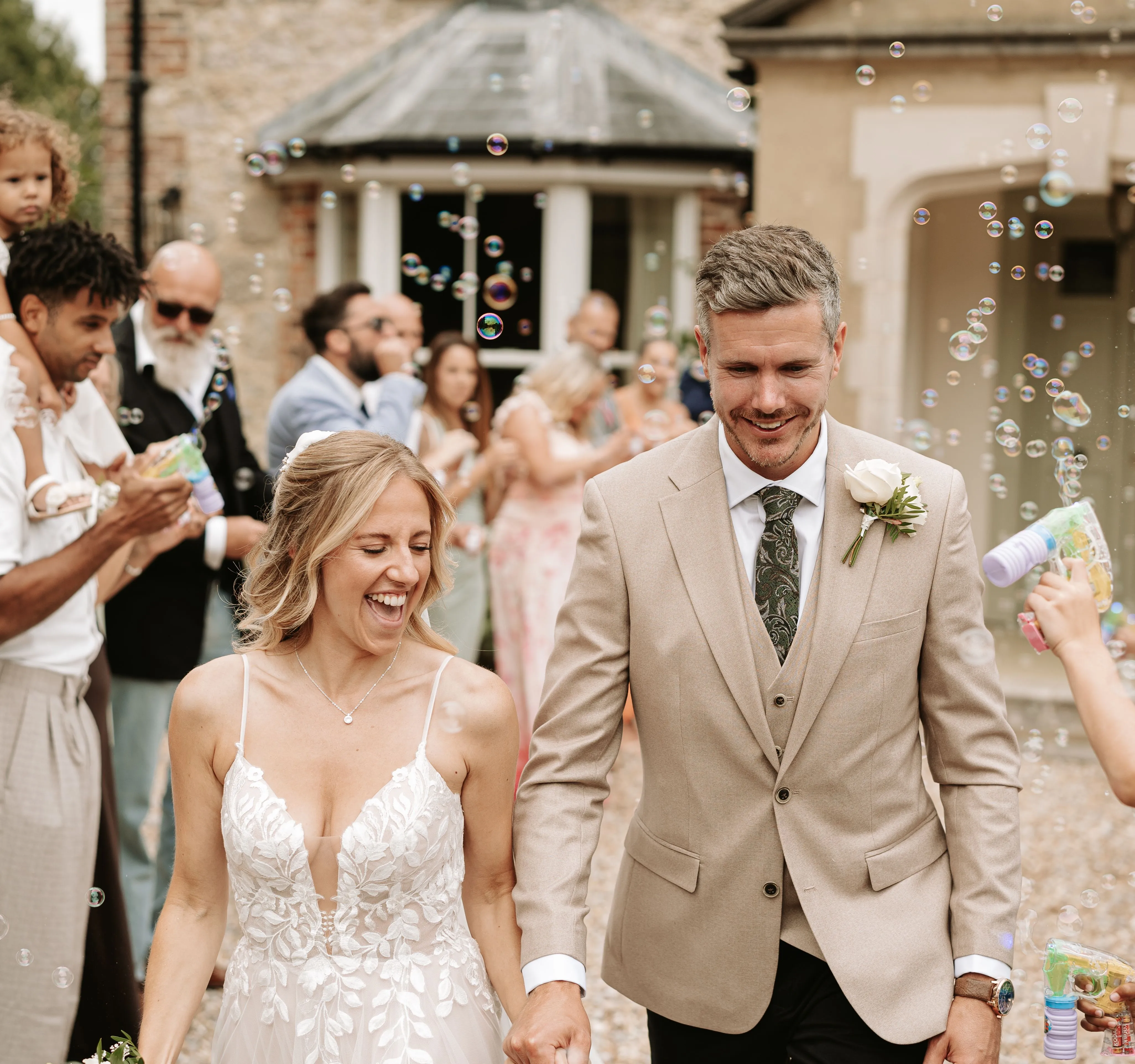 Bride and groom walk hand in hand through guests blowing bubbles outside a country house wedding venue