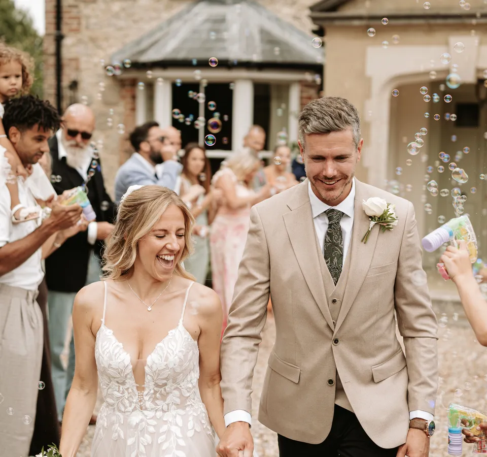 Bride and groom walk hand in hand through guests blowing bubbles outside a country house wedding venue