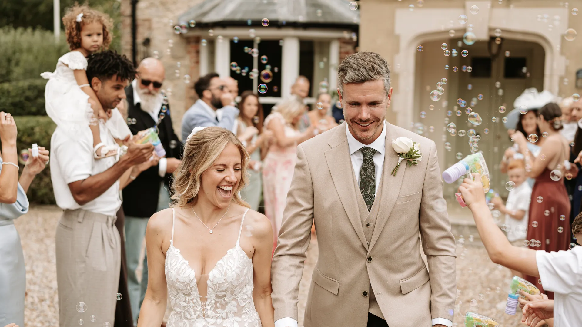 Bride and groom walk hand in hand through guests blowing bubbles outside a country house wedding venue