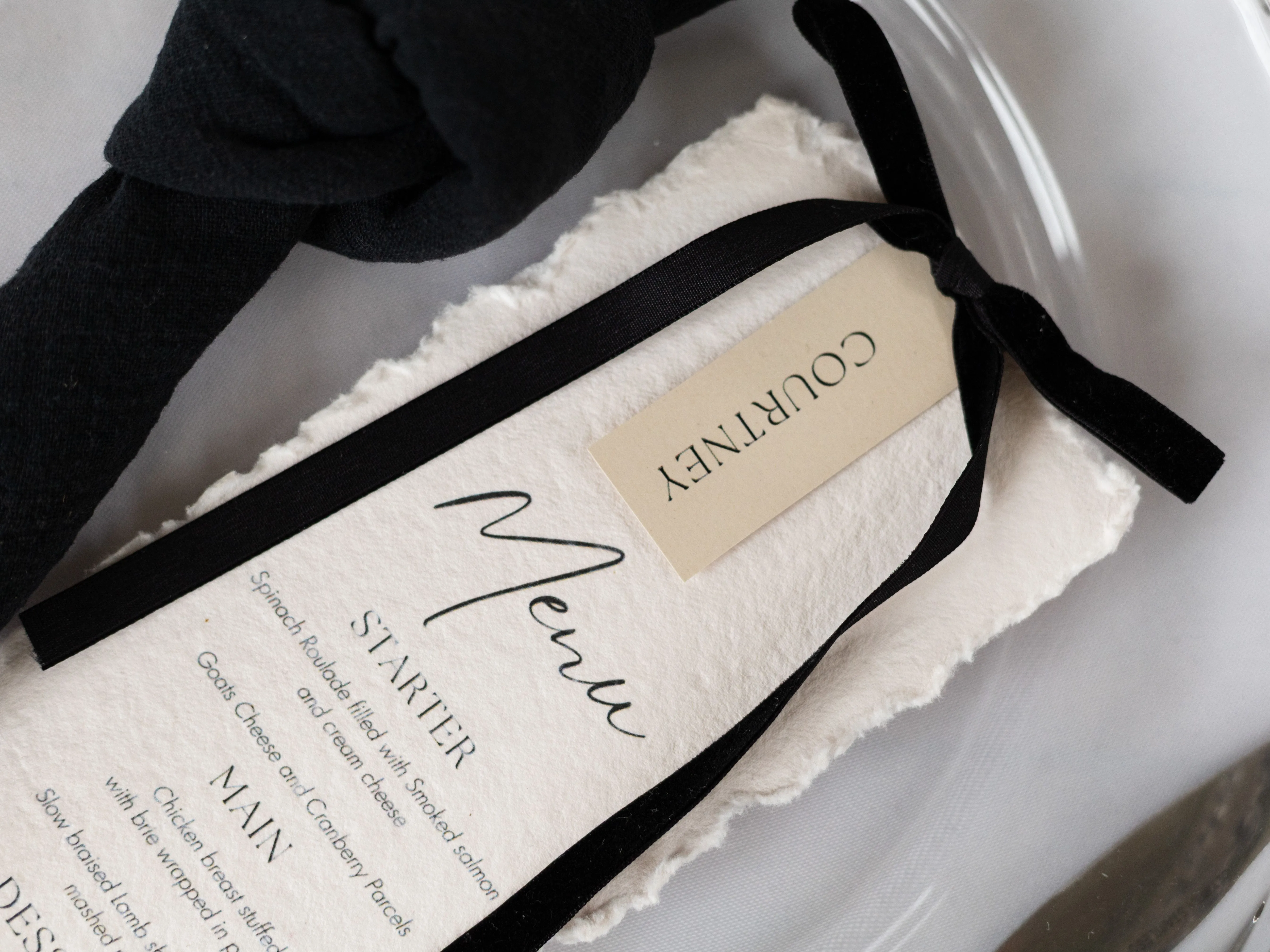 Wedding menu on textured paper tied with a black ribbon, beside white roller skates and a black bow accessory.