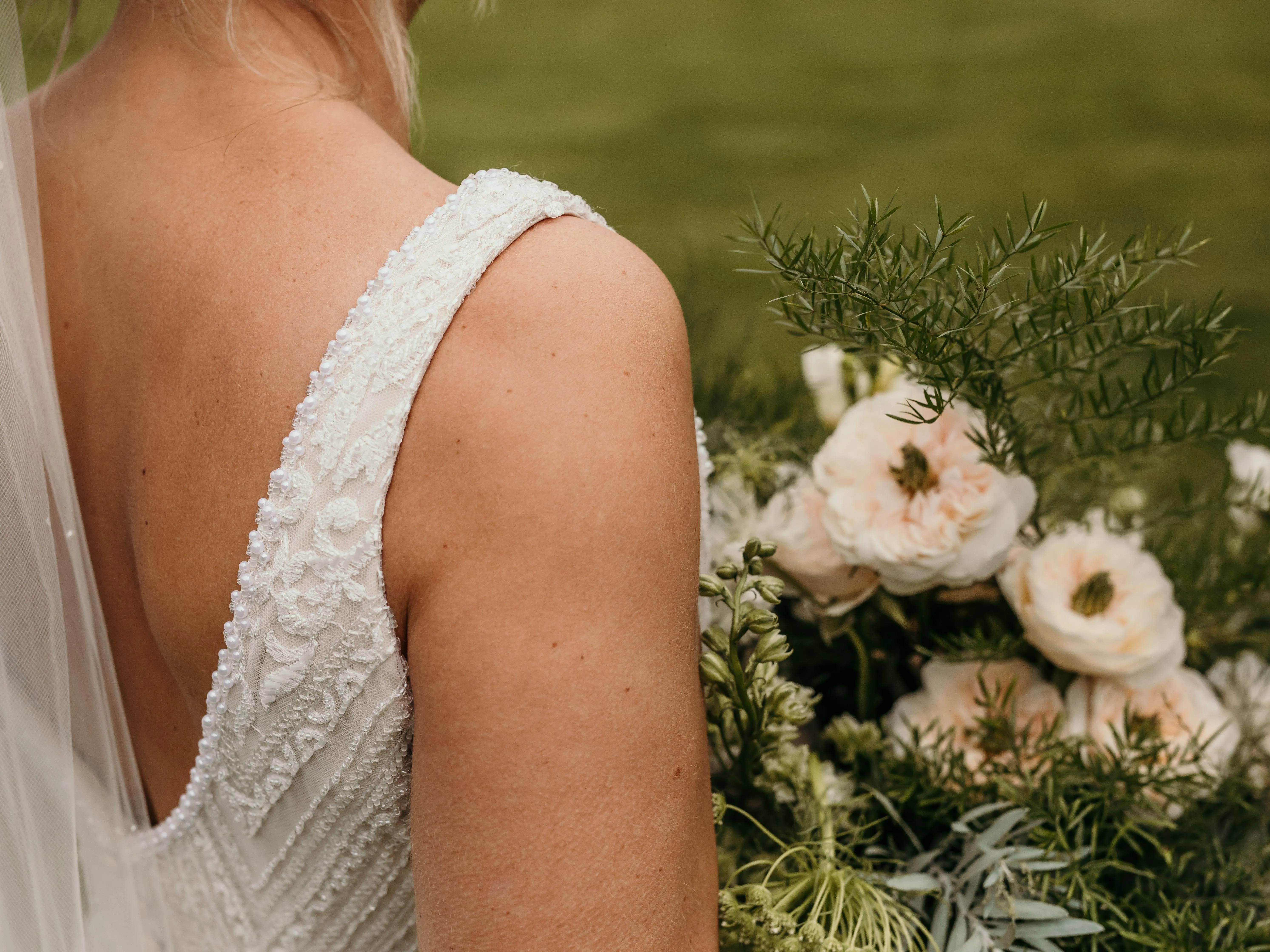 Close-up of bride in lace wedding dress holding a bouquet of pale roses and greenery