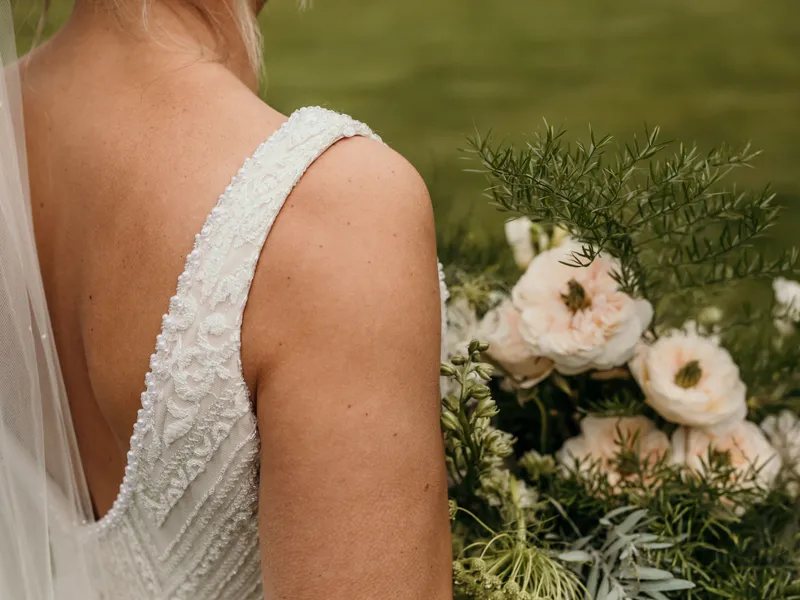 Close-up of bride in lace wedding dress holding a bouquet of pale roses and greenery