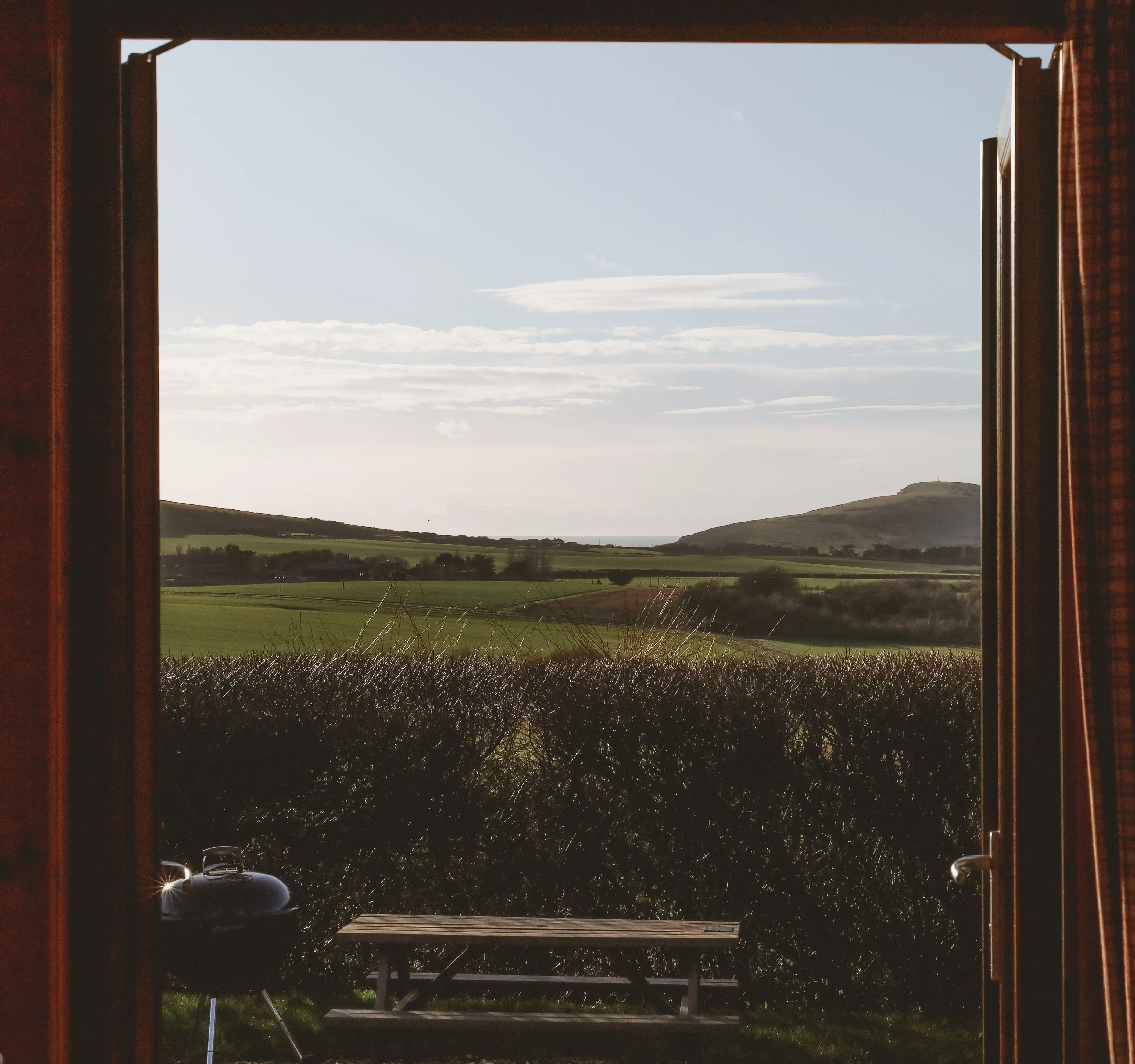 View through an open cabin door to green fields and distant hills under a pale blue sky