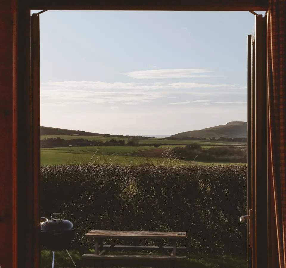 View through an open cabin door to green fields and distant hills under a pale blue sky