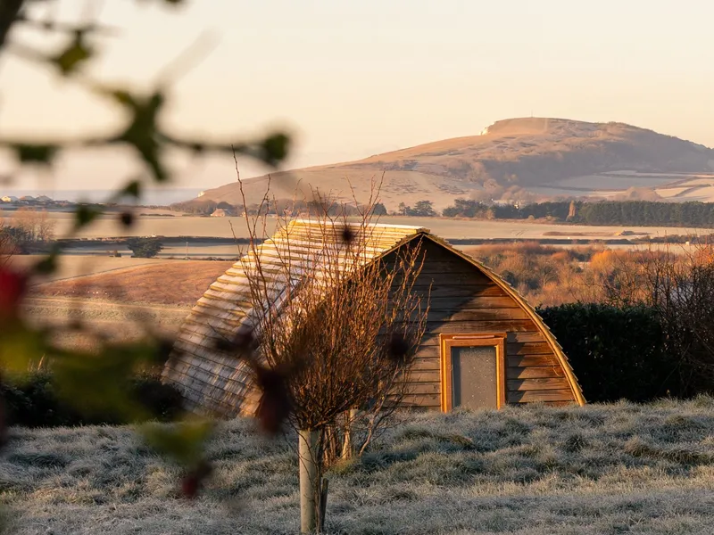 Wooden pod cabin in a frosty field with hills in the background at sunrise