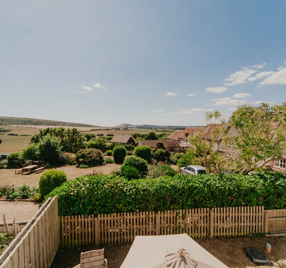 View through open window over cottage garden and countryside fields under a blue sky
