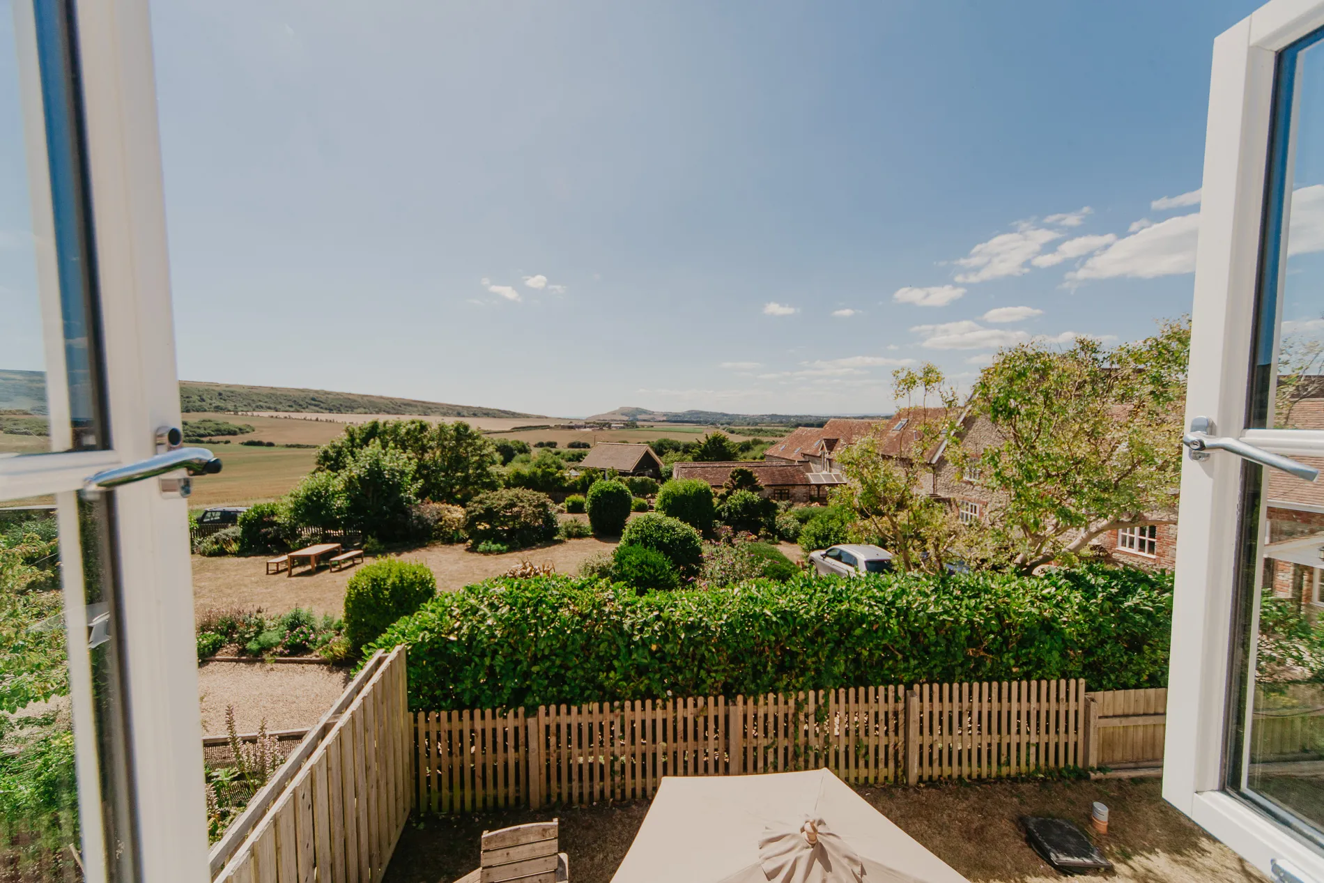 View through open window over cottage garden and countryside fields under a blue sky