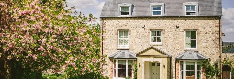 Stone country house with slate roof and bay windows beside a blooming pink tree