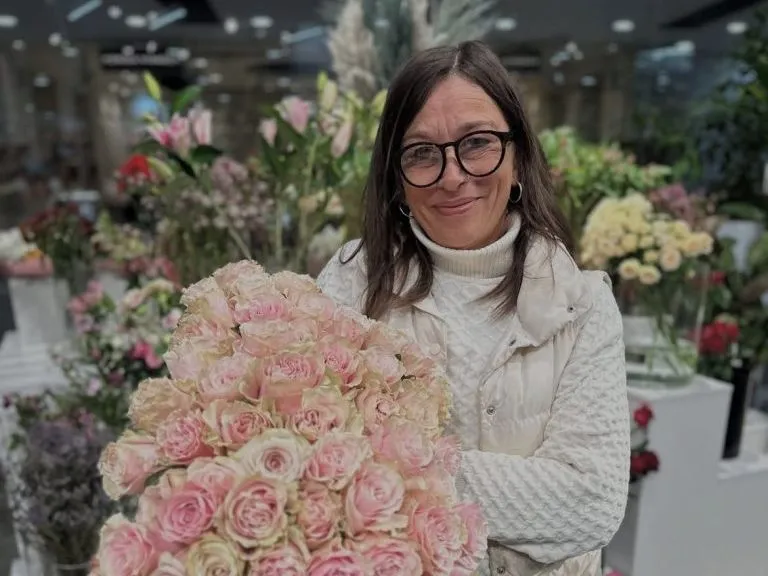 Woman wearing glasses holding a large bouquet of pale pink roses in a flower shop