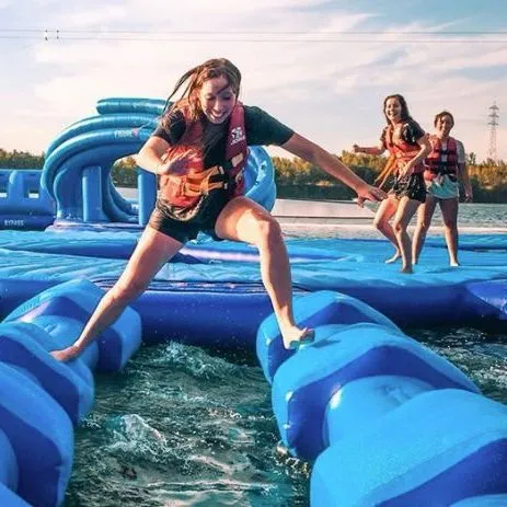 People wearing life jackets playing on a blue inflatable water obstacle course on a lake