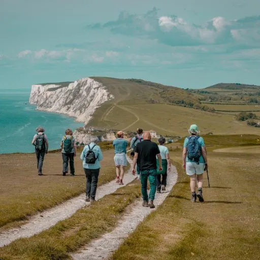 Group of hikers walking along a coastal path towards white chalk cliffs overlooking the sea