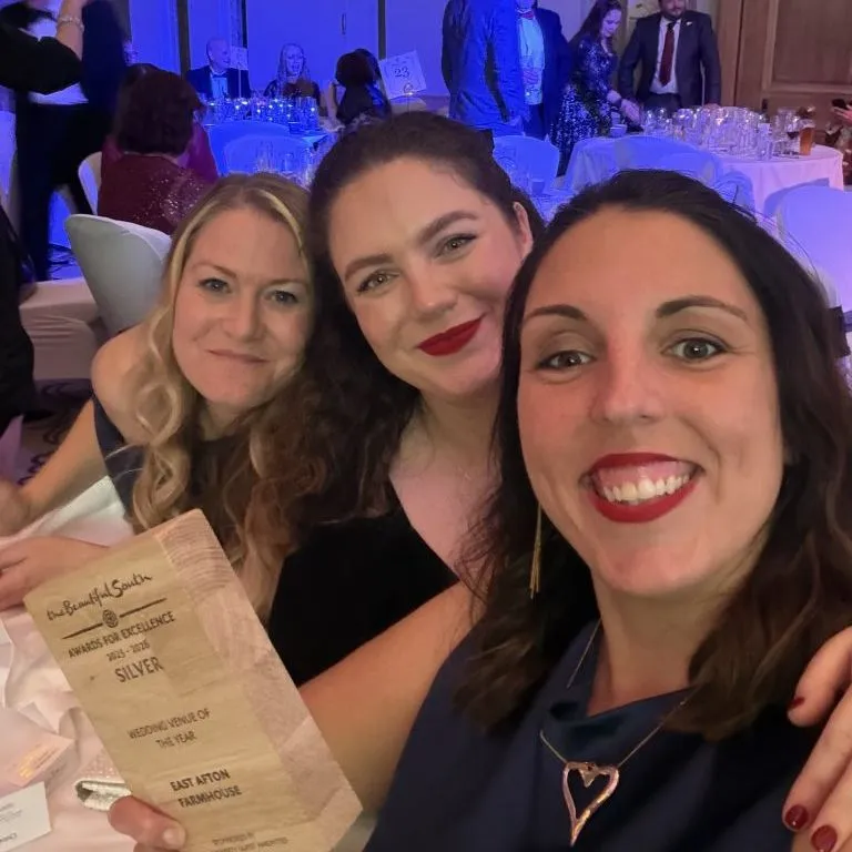 Three women smiling for a selfie at an awards dinner, holding a Silver award certificate.