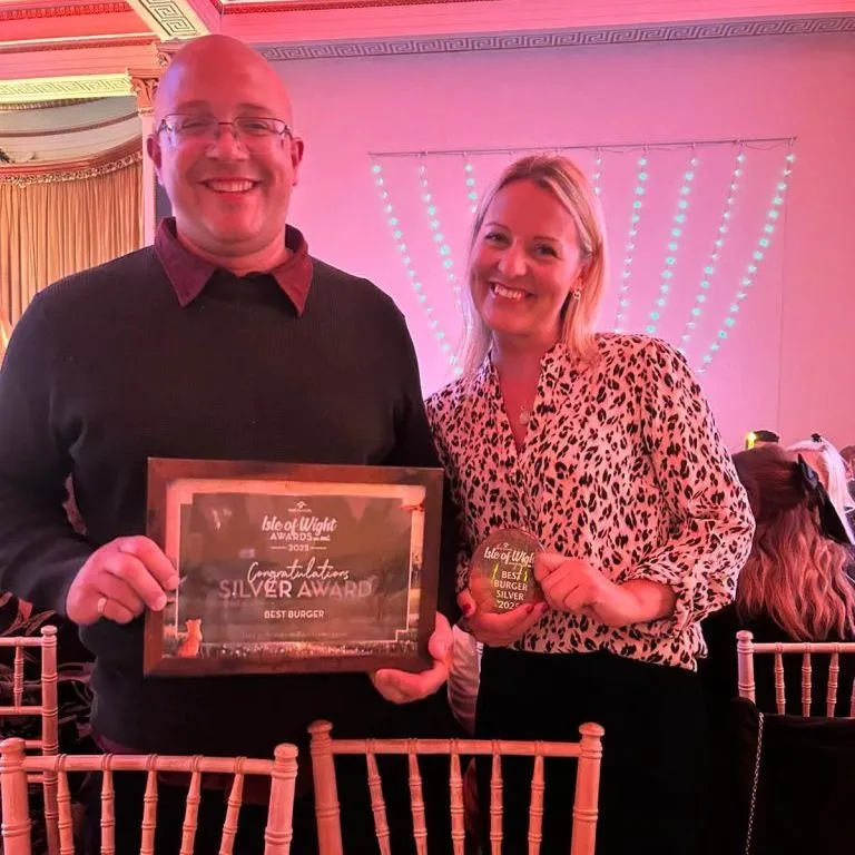 Two people smiling at an awards event, holding a framed Silver Award certificate and a trophy