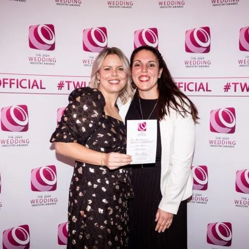 Two women holding an award certificate in front of The Wedding Industry Awards 2024 backdrop