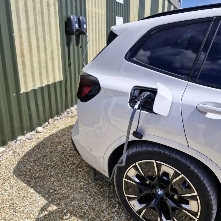 Electric car charging from wall-mounted EV charger beside a corrugated metal building
