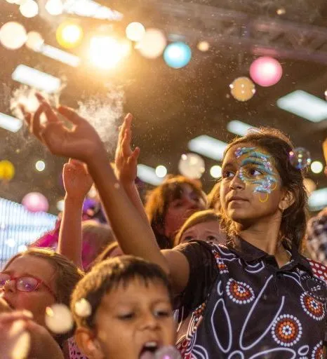 Children dancing under colourful lights and bubbles at a kids’ rave, with face paint and raised hands