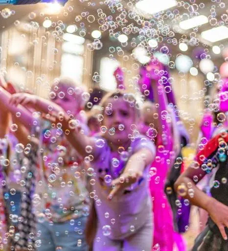 Children dancing at an indoor kids rave surrounded by bubbles