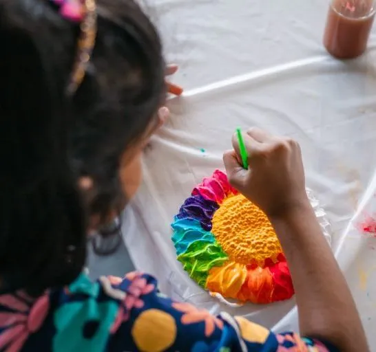 Child painting a brightly coloured sunflower craft at a table