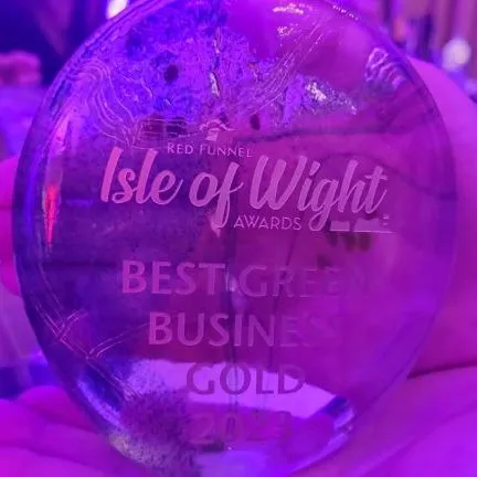 Hand holding a glass award engraved “Isle of Wight Awards” and “Best Green Business Gold 2023”