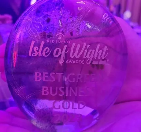 Hand holding a glass award engraved “Isle of Wight Awards” and “Best Green Business Gold 2023”