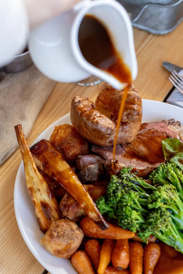 Gravy being poured over a traditional Sunday roast with vegetables, Yorkshire pudding, and meat